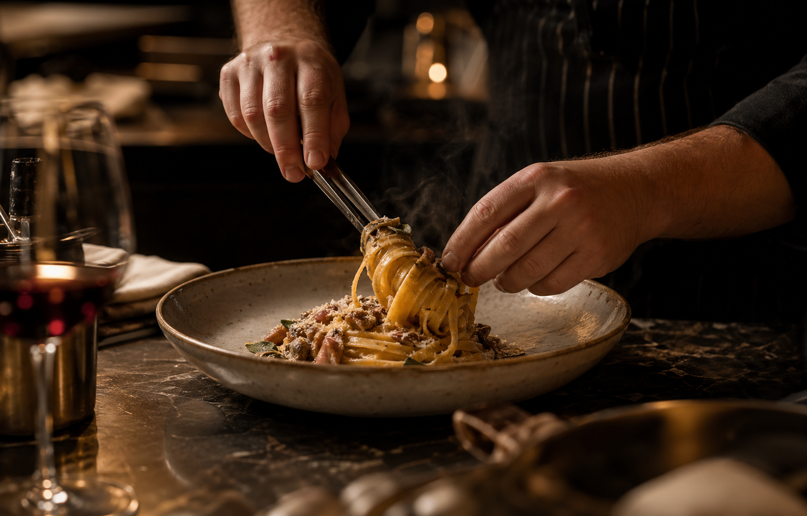 Chef hands finishing a refined pasta dish at an intimate counter.